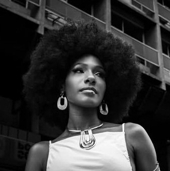 Retrato de mulher com cabelo black power diante de um prédio