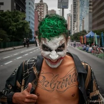 Homem com maquiagem de palhaço e cabelo verde no meio da avenida